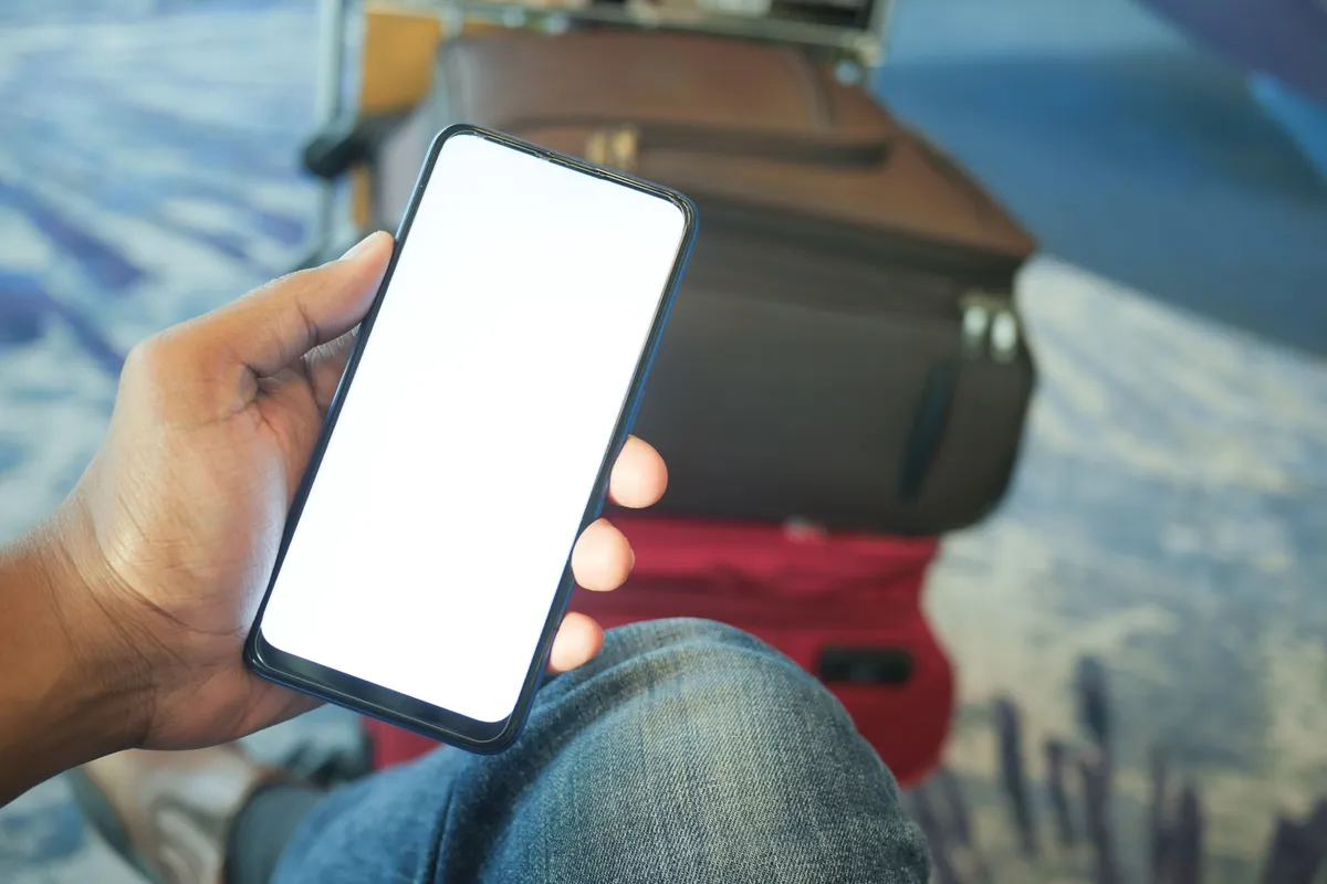 Viajero con el móvil en la mano y las maletas al lado, esperando en el aeropuerto