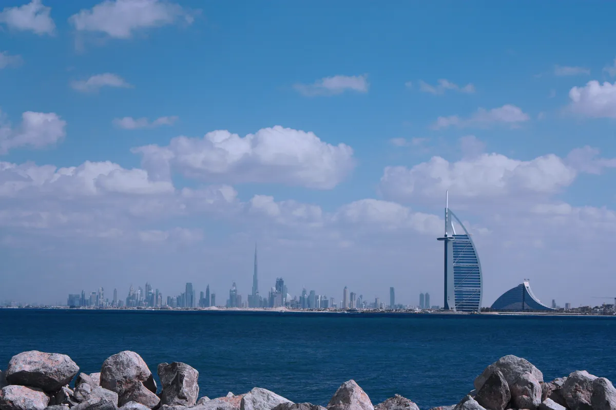 El perfil de Dubái al otro lado del mar, con el Burj Khalifa a lo lejos y el Burj Al Arab con forma de vela a la derecha, visto desde una orilla de rocas